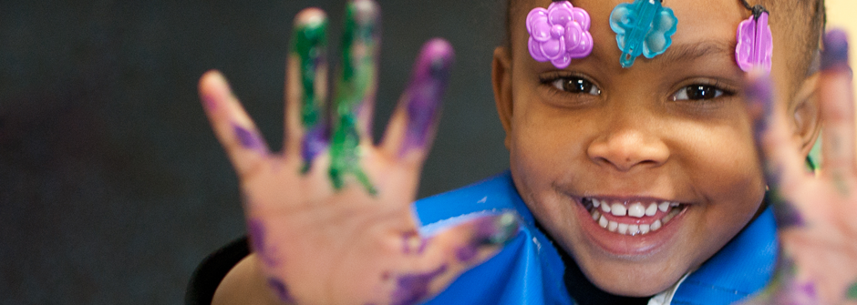 close-up: toddler smiling, showing us her open hands to covered in paint