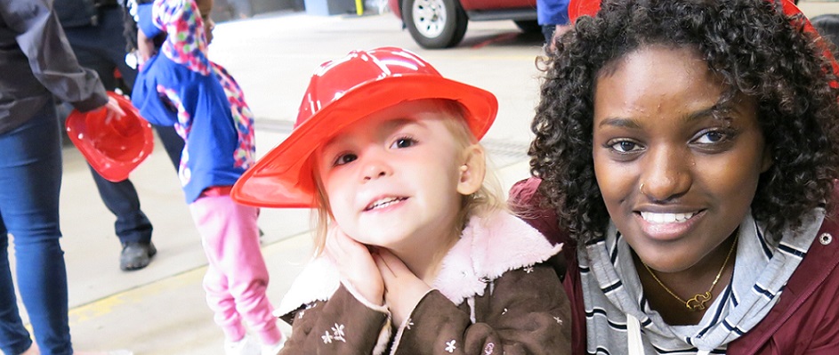 child in kid's firefighter hat posing with smiling woman