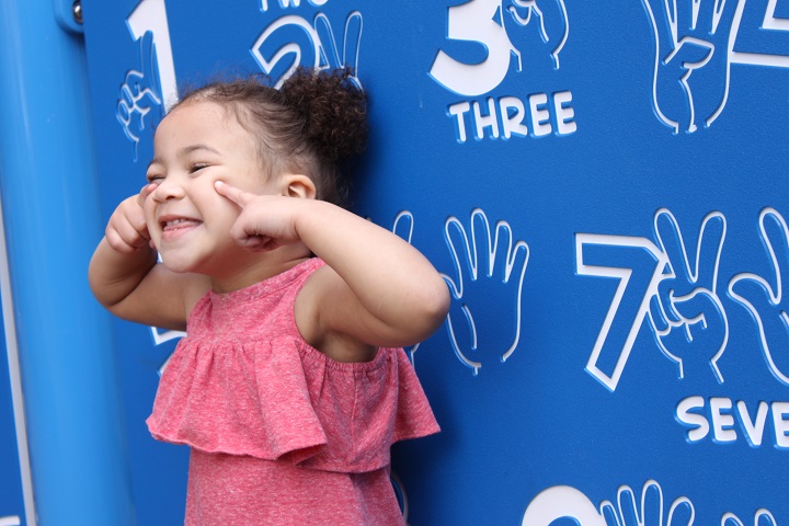 Girl with gleeful smile in front of activity board at new playground.