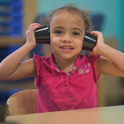 preschooler posing with cups on her ears