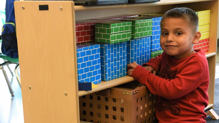 Close-up of preschool boy posing at shelves of building blocks