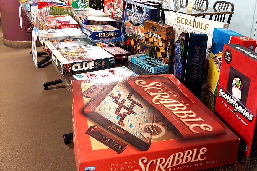 A table filled with various board games, including Scrabble, Clue, Scattergories, and Battleship.