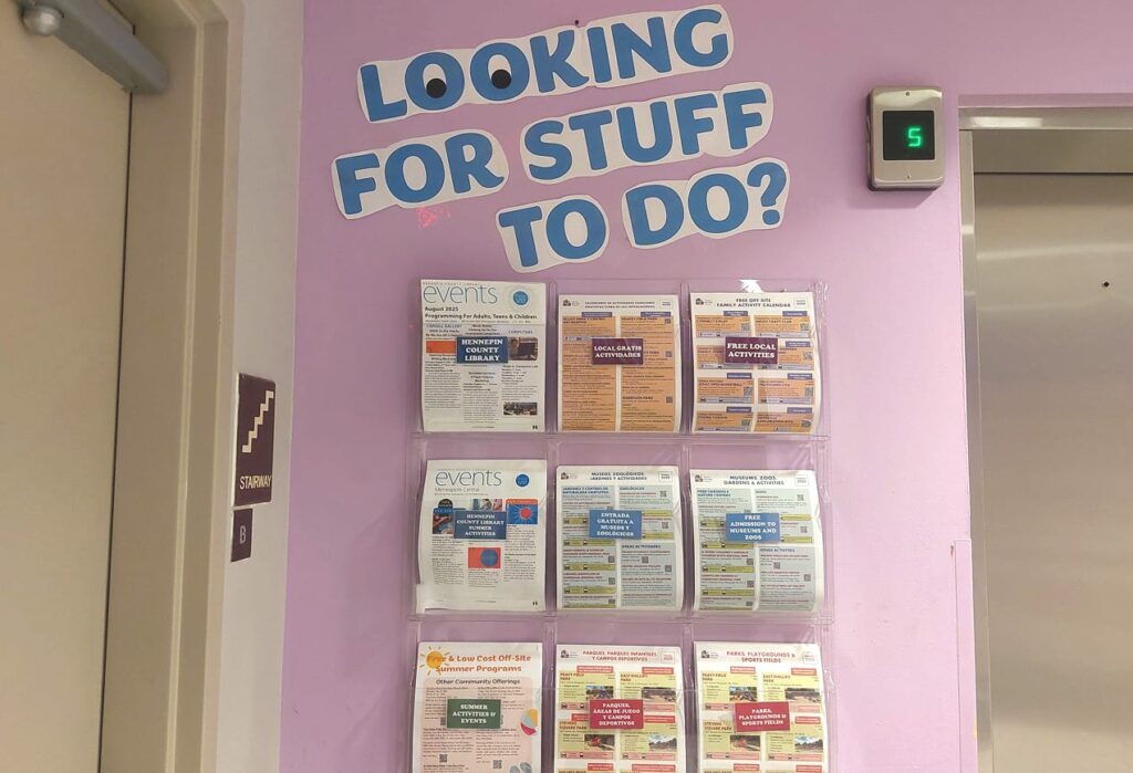 Wall with a sign saying “Looking for stuff to do?” above racks of event flyers and a nearby elevator with a green "5" display.