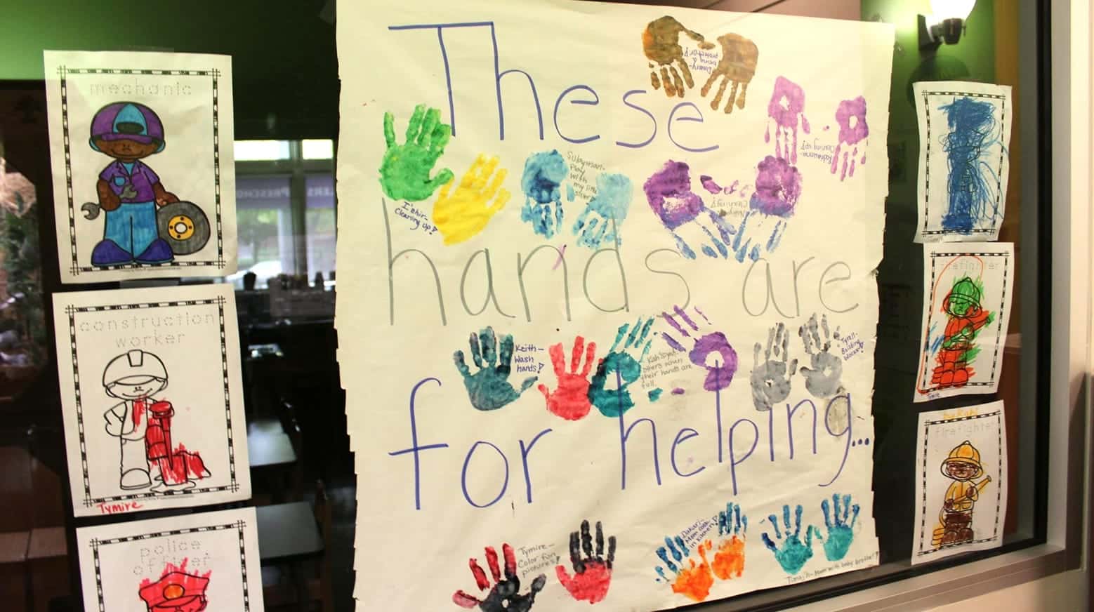A poster with colorful handprints reads "These hands are for helping," surrounded by children's drawings of community helpers.