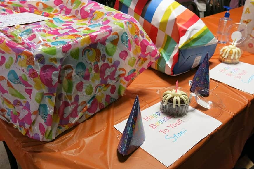 A birthday table with gifts, party hats, cupcakes with candles, and colorful balloon-themed decorations.
