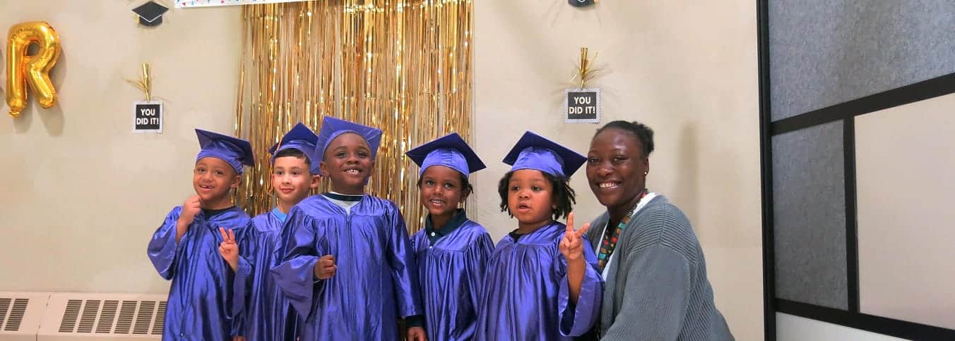 Five children in purple graduation gowns and a smiling woman pose together at a celebration with gold decorations.