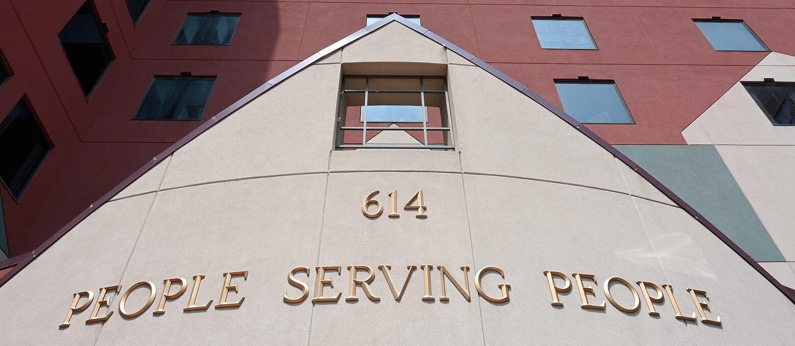 Building facade with large gold letters reading “614 PEOPLE SERVING PEOPLE” beneath a window, against a red and beige wall.