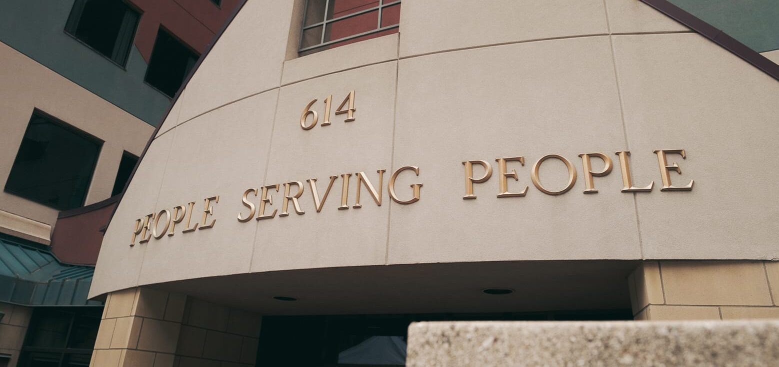 A beige building facade with the words "PEOPLE SERVING PEOPLE" and the number 614 above the entrance.
