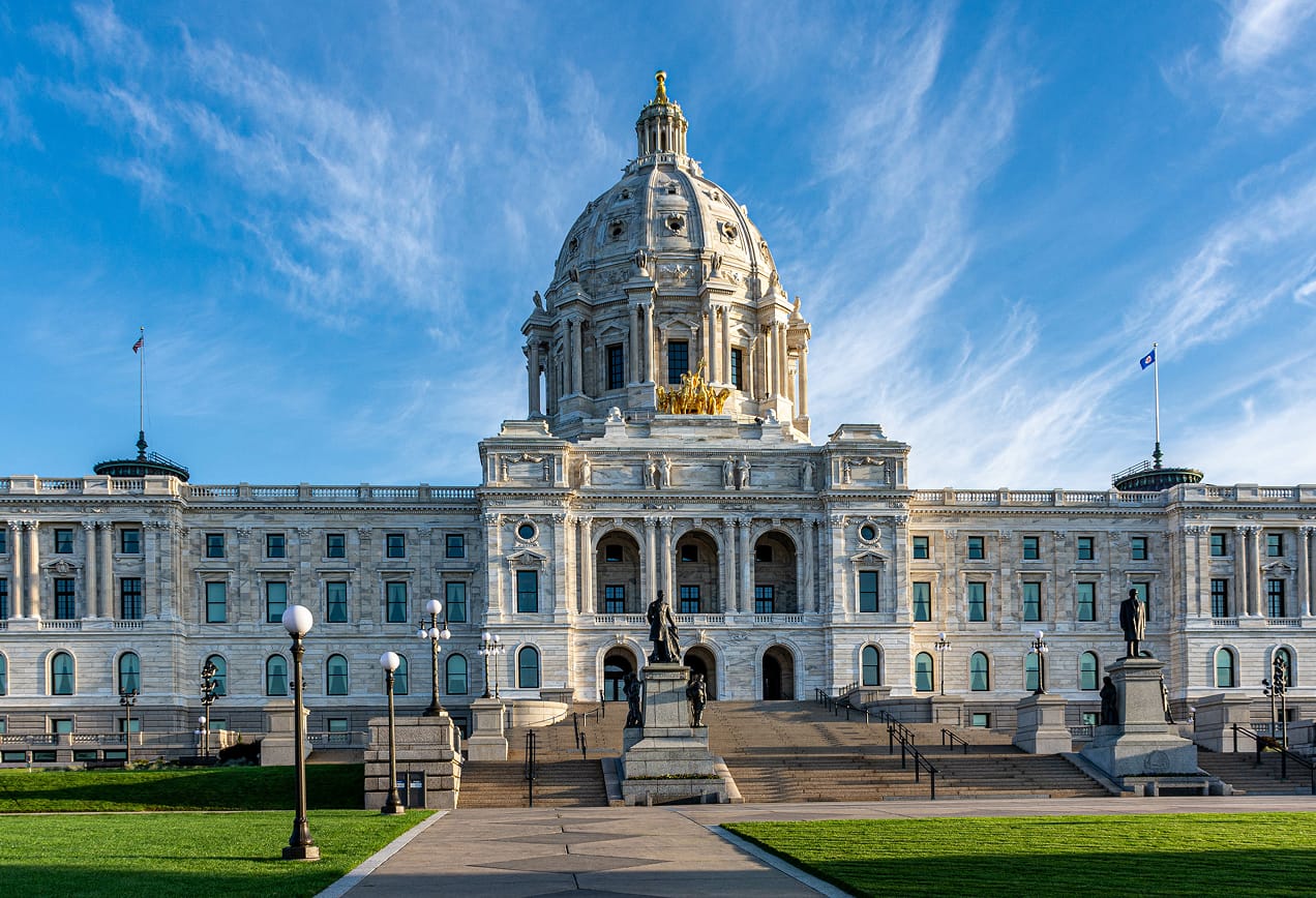 The Minnesota State Capitol building with a central dome, statues, and a blue sky in the background.