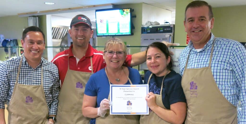 5 men and woman in aprons standing in a line in front of kitchen at People Serving People