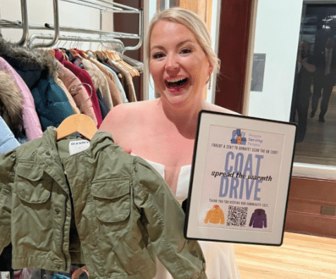 picture of woman holding up child's coat on hanger and sign that says coat drive