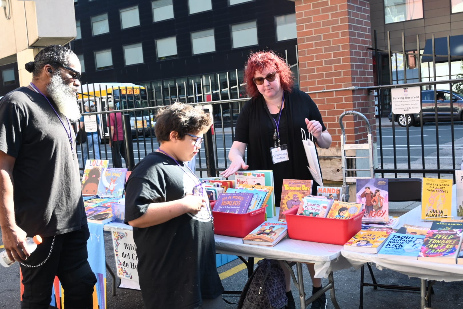 Father and son looking at table of books with Hennepin County library staff behind table