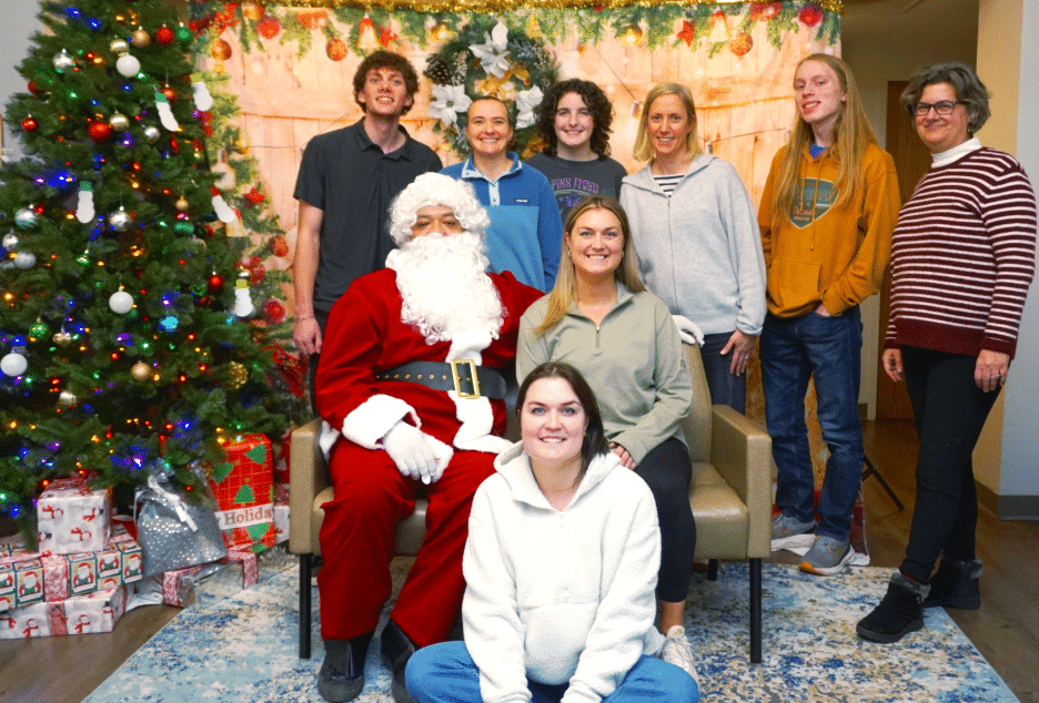 group of volunteers standing around seated Santa Claus