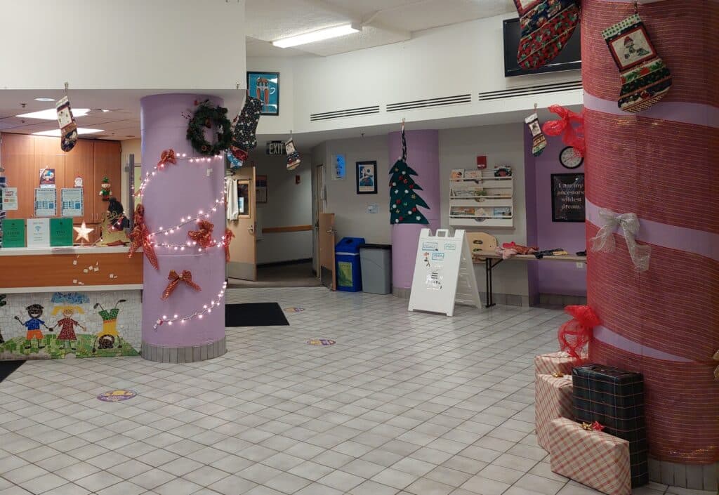 The lobby of People Serving People's downtown shelter is decorated for winter holidays. Light purple columns are adorned with bows, wrapping paper, and white lights. Stockings hang from the ceiling and wrapped presents sit under a column.
