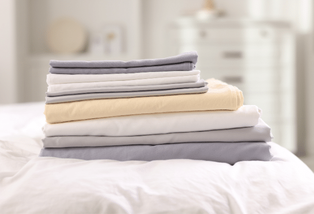 A stack of grey and beige linen on a white bed.