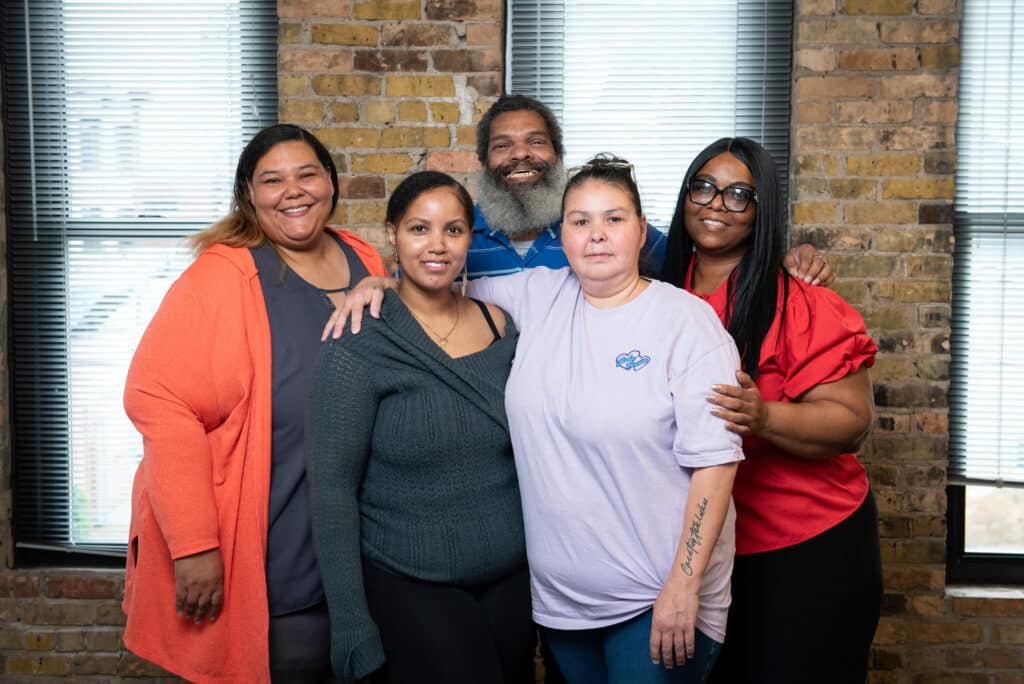 Group of 5 people standing with arms around each other